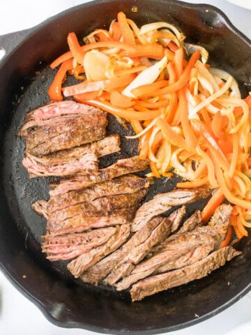 sliced steak, peppers and onions in a cast iron skillet