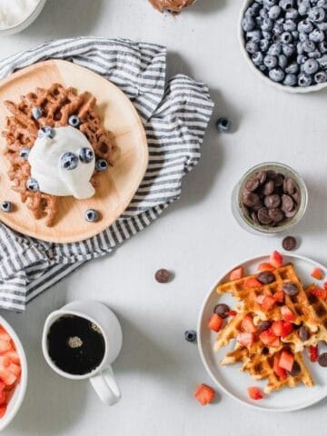 waffles and toppings on plates and in bowls on a table