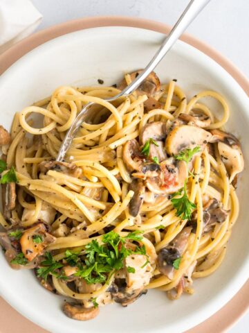 close up of pasta with mushrooms, bacon, and chicken with a fork in it