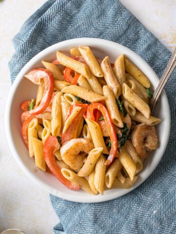 close up of penne pasta with shrimp and bell peppers in a white bowl